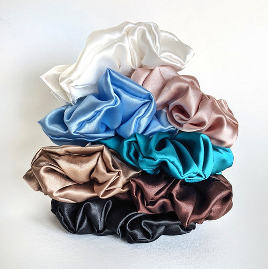 A pile of large satin scrunchies in various colours.